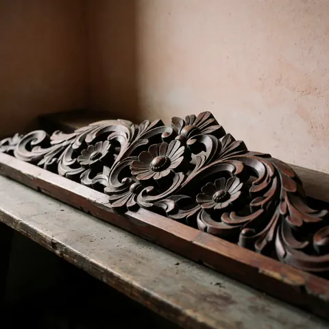Détail d'une moulure décorative de style colonial en bois foncé, ornée de motifs floraux sculptés à la main avec un relief prononcé.