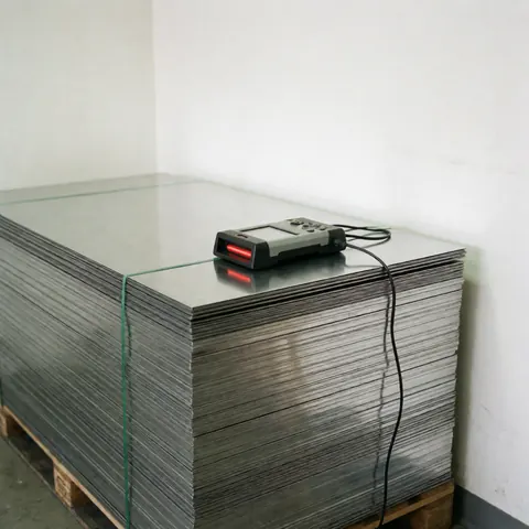 Pile ordonnée de tôles métalliques posée sur une palette avec un scanner au-dessus, dans un environnement industriel aux murs blancs et à l'éclairage clair.