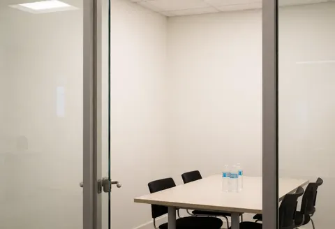 Salle de réunion vide avec table, chaises noires, bouteilles d'eau et murs blancs, idéale pour les ONG et les communautés.