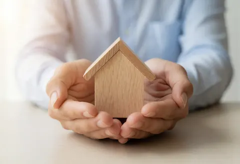 Des mains tenant une petite maison en bois symbolisant la protection et la sécurité du logement dans le secteur des assurances.
