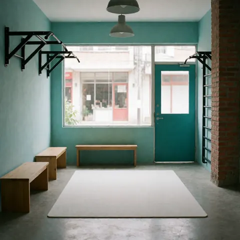 Vue d'un espace fitness minimaliste avec bancs en bois, tapis de sol, murs turquoise, pilier en briques et éclairage suspendu.