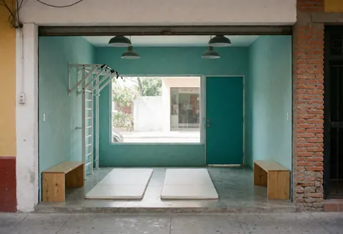 Vue d'un petit gymnase avec murs turquoise, sol gris, bancs en bois et luminaires industriels, idéal pour l'entraînement.