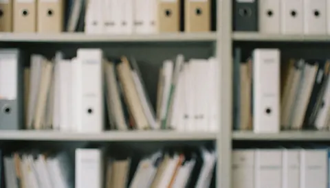 Étagère métallique grise remplie de classeurs et de fichiers blancs, servant de fond professionnel neutre pour des présentations ou documents liés aux ressources humaines.