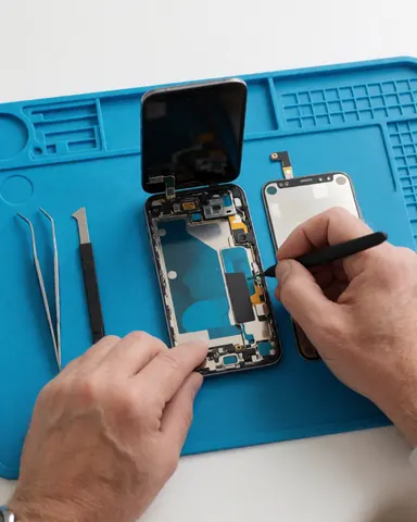 Vue détaillée d'outils de réparation pour smartphones disposés sur une surface blanche avec un tapis bleu, incluant pinces et tournevis.