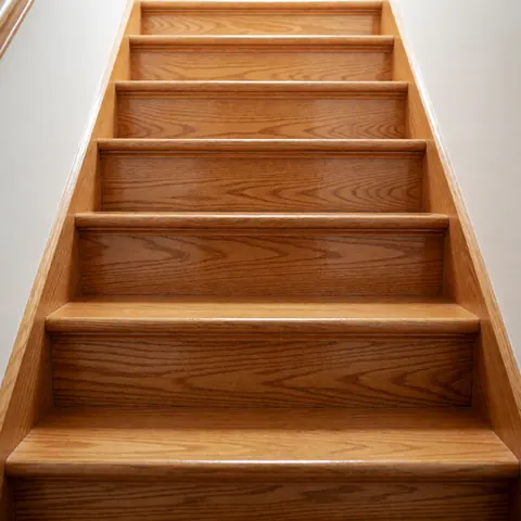 Vue rapprochée d'un escalier en bois clair restauré, avec une surface polie et brillante reflétant la lumière dans un intérieur de maison.