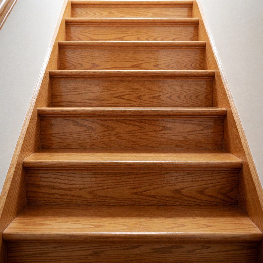 Vue rapprochée d'un escalier en bois clair restauré, avec une surface polie et brillante reflétant la lumière dans un intérieur de maison.