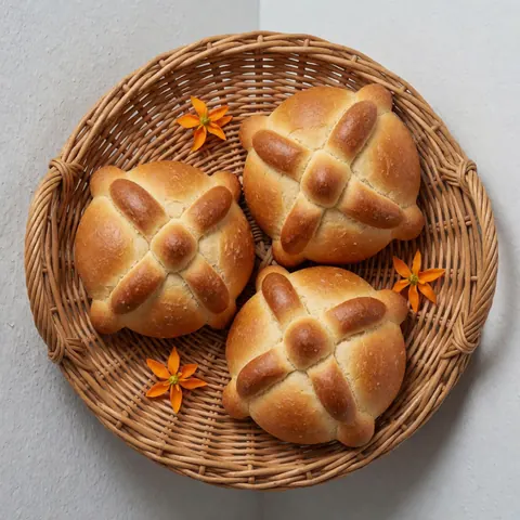 Un panier en osier rempli de pains traditionnels espagnols décorés de croix, accompagnés de fleurs orange.