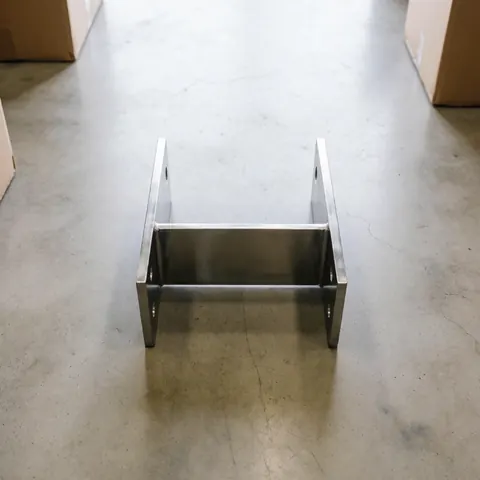Support métallique poli et précis sur sol en béton dans une usine, éclairage diffus, scène industrielle propre et réaliste.
