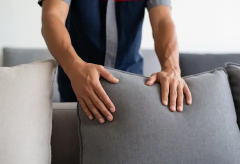 Un homme ajuste soigneusement un coussin sur un canapé gris dans un magasin de meubles, illustrant un service professionnel en action.