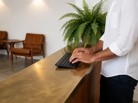 Un homme travaille au clavier sur un bureau moderne en bois et bronze, avec une plante verte, dans un intérieur élégant et lumineux.