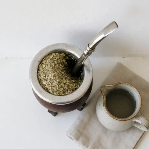 Gourde traditionnelle remplie de yerba mate avec une bombilla, accompagnée d'une carafe d'eau chaude et d'un tissu sur une table.