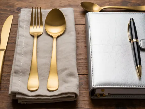 Couverts argent et or, serviette et agenda sur table en bois, idéal pour planifier mariages élégants.