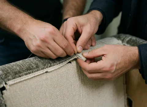 Gros plan montrant des mains expertes en train de coudre du tissu pour la rénovation ou la fabrication de meubles d'ameublement avec précision et soin.