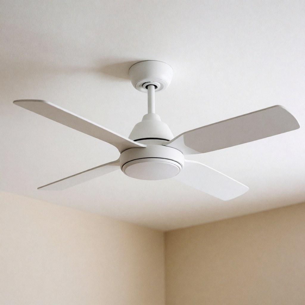 Vue en contre-plongée d'un ventilateur de plafond moderne et minimaliste installé sur un plafond blanc dans une pièce aux murs beige, éclairée naturellement.