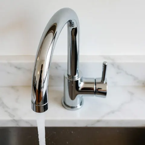 Un robinet en acier inoxydable installé proprement sur un plan de travail en marbre blanc dans une cuisine moderne, reflétant la lumière et soulignant la fraîcheur du design.