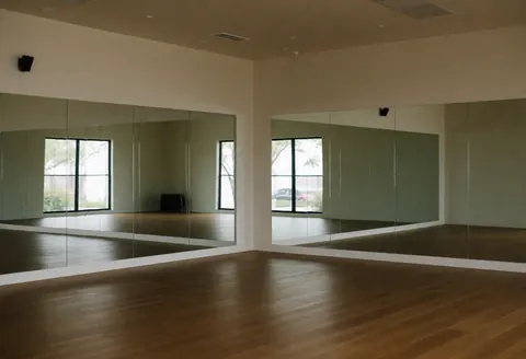 Studio de yoga vide avec miroirs et sol en bois, baigné de lumière naturelle. Ambiance calme et spacieuse, idéale pour les salles de sport et centres de bien-être.