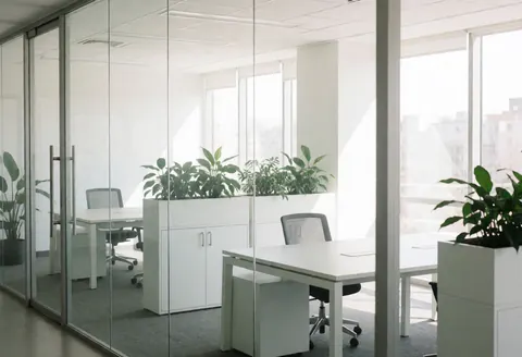 Intérieur d'un bureau moderne et minimaliste pour startups, avec bureaux vides, plantes vertes, murs vitrés et lumière naturelle entrant par les grandes fenêtres.