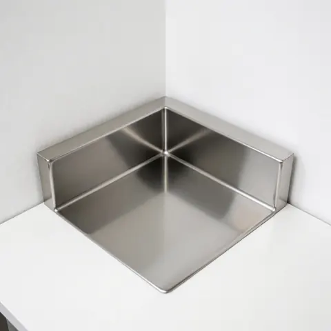 Vue rapprochée d'un évier industriel en acier inoxydable installé dans un coin, avec une surface blanche réfléchissante et un design moderne.