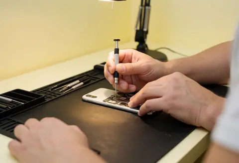 Technicien effectuant une réparation sur un téléphone portable avec des outils spécialisés.