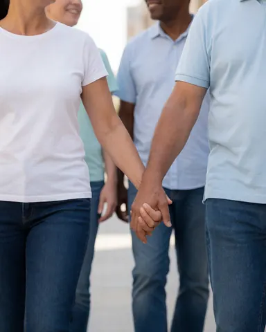 Un couple souriant se promène main dans la main dans une rue urbaine avec des piétons flous en arrière-plan.