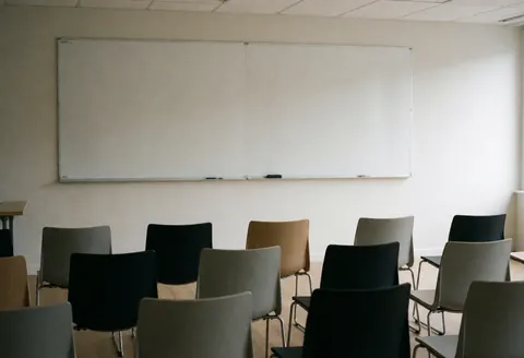 Salle de formation moderne et vide équipée de chaises et d'un tableau blanc, idéale pour présentations, réunions ou formations professionnelles.