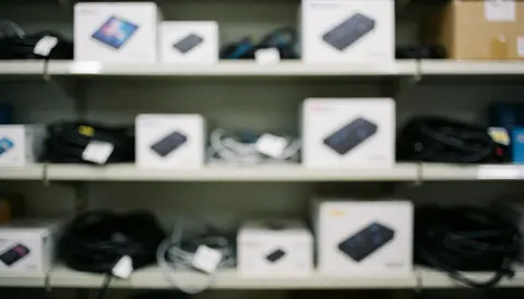 Arrière-plan flou d'un entrepôt technologique montrant des étagères remplies de boîtes contenant des appareils électroniques, idéal pour du texte professionnel.