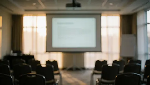 Vue d'une salle de réunion professionnelle équipée d'un projecteur, d'un grand écran blanc, de chaises alignées et de fenêtres laissant entrer la lumière naturelle.