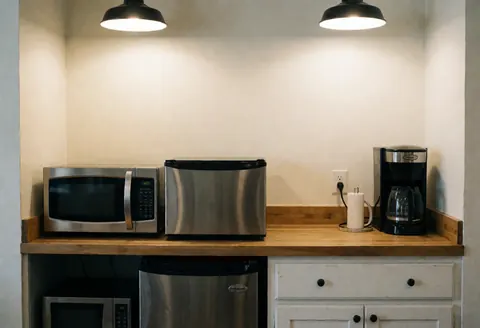 Cuisine d'office dotée d'un micro-ondes, d'un réfrigérateur et d'une cafetière posés sur une table en bois, murs chaleureux et éclairage plafond.