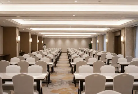 Vue d'une salle de réception spacieuse et lumineuse, meublée de tables rondes et de chaises blanches prêtes pour un événement.