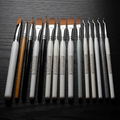 Pinceaux et outils de nail art professionnels disposés sur une table en bois sombre avec un éclairage dramatique et contrasté.