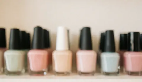 Arrière-plan flou et pastel composé de plusieurs flacons de vernis à ongles disposés sur une surface claire, créant une texture douce et apaisante pour un design.