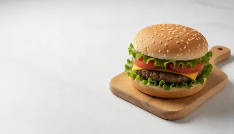 Un hamburger avec laitue, tomate et fromage posé sur une planche en bois, sur fond blanc, idéal pour menus et bannières de restauration rapide.