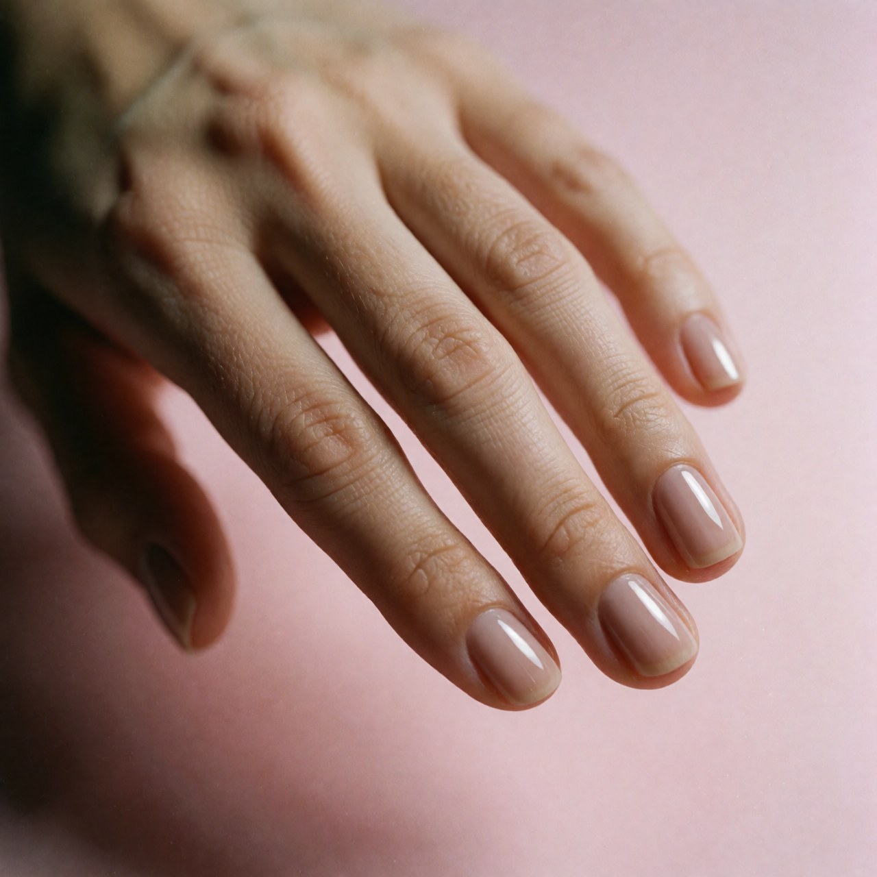 Main féminine présentant une manucure en gel parfaitement réalisée avec un fini brillant sur fond rose.