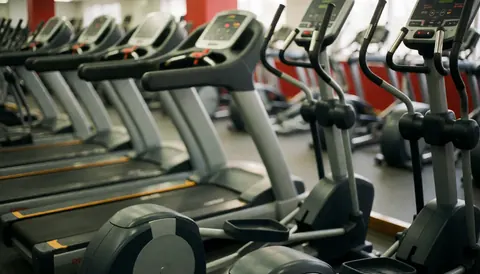 Arrière-plan abstrait et flouté d'une salle de fitness moderne avec des tapis de course et des machines elliptiques aux tons gris et rouge, idéal pour des textes promotionnels.