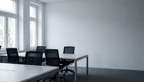 Espace de travail moderne et épuré avec tables et chaises vides, murs gris et lumière naturelle, idéal pour ajouter du texte ou un logo.