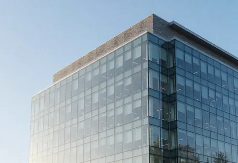 Façade en verre d'un immeuble de bureaux contemporain reflétant le ciel bleu, évoquant la transparence et le professionnalisme pour les cabinets comptables.