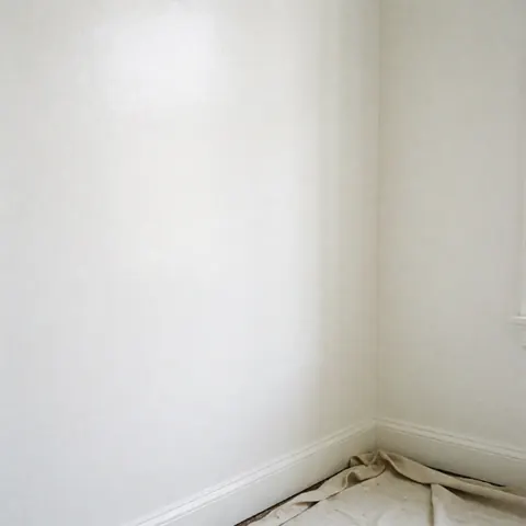 Vue aérienne d'un mur intérieur peint en blanc brillant avec une plinthe, une bâche protectrice au sol et un fini impeccable pour décoration ou rénovation.