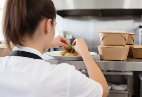 Un chef cuisinier en train de garnir et d'assaisonner un plat blanc avec soin dans une cuisine professionnelle équipée d'inox.