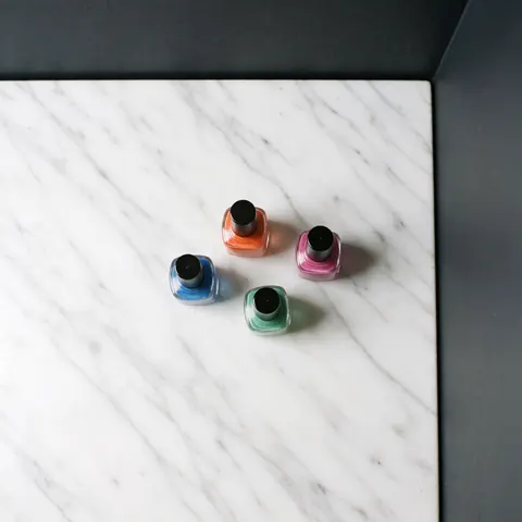 Plusieurs bouteilles d'émail à ongles aux couleurs vives disposées sur une surface en marbre blanc poli, éclairage studio pour photographie de produit.