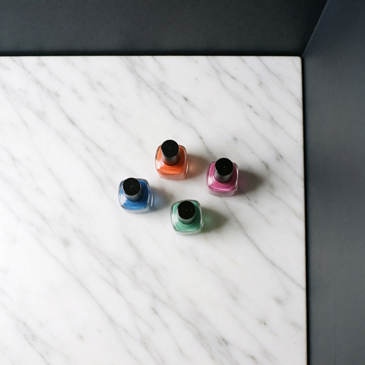 Plusieurs bouteilles d'émail à ongles aux couleurs vives disposées sur une surface en marbre blanc poli, éclairage studio pour photographie de produit.