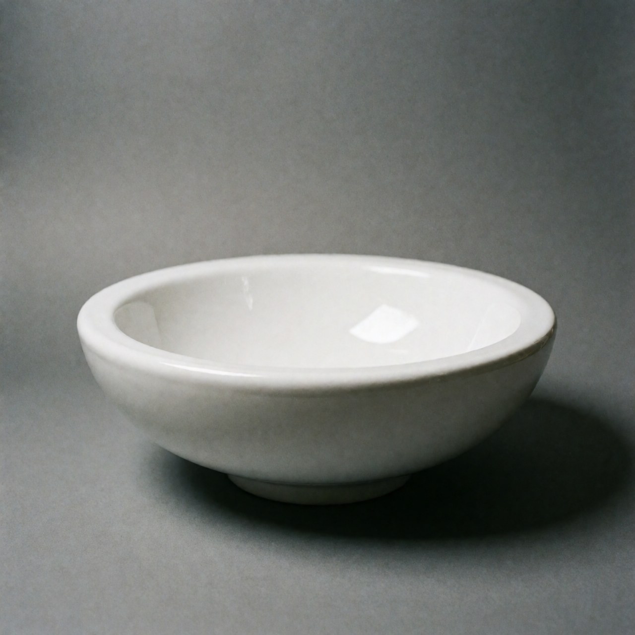 Un évier en céramique blanche posé sur un fond gris avec une illumination douce et minimaliste, idéal pour la décoration de salle de bain ou cuisine.