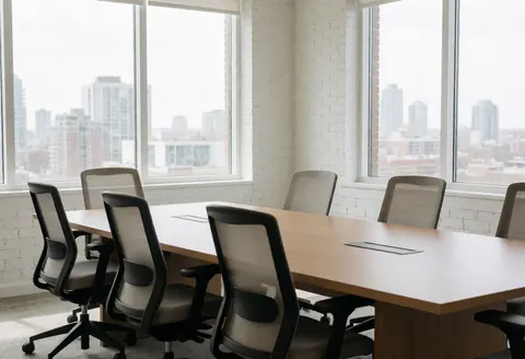 Salle de réunion professionnelle équipée d'une longue table en bois, de chaises ergonomiques, de murs en briques blanches et de grandes fenêtres offrant une vue panoramique sur la ville.