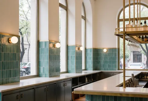 Intérieur d'un bar moderne avec des carreaux turquoise, des détails en bronze, de grandes fenêtres et un comptoir épuré, éclairage chaleureux et ambiance élégante sans personnes.
