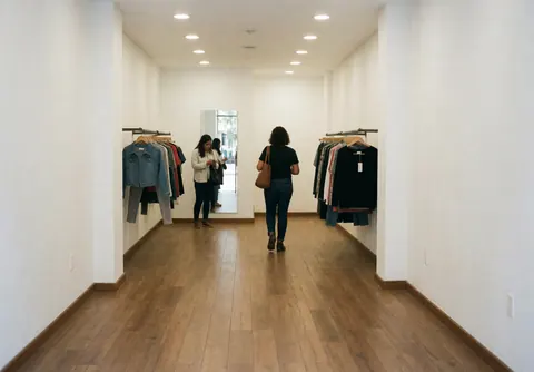 Vue intérieure d'une boutique de mode contemporaine aux murs blancs et au sol en bois clair, éclairée naturellement.