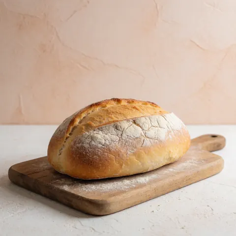 Une tranche de pain artisanal à la croûte dorée est présentée sur une planche en bois rustique, avec un fond clair et un mur terracotta en arrière-plan.