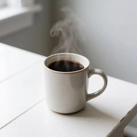 Une tasse en céramique contenant du café chaud dégageant de la vapeur, posée sur une surface blanche lisse et propre.