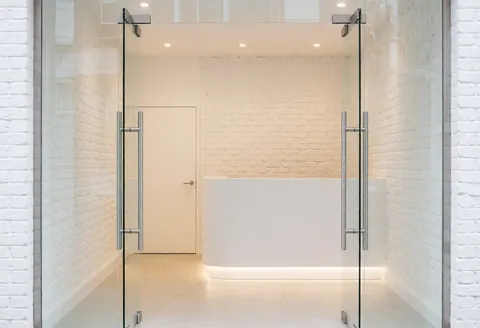 Façade en verre et murs en briques blanches d'une salle de sport contemporaine, éclairage chaleureux et espace minimaliste.