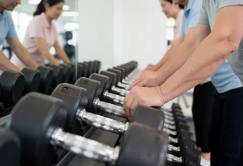 Une rangée d'haltères alignés sur un support en métal au sein d'un gymnase moderne, avec des équipements de fitness en arrière-plan.