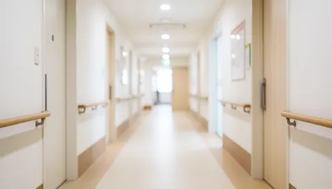 Vue floue d'un couloir lumineux et propre d'une clinique avec des murs blancs et une rampe, évoquant un environnement médical calme et professionnel.