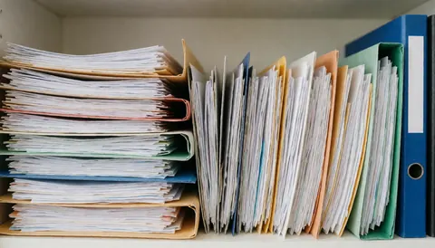 Des classeurs et dossiers aux couleurs vives sont rangés sur une étagère blanche, offrant un arrière-plan idéal pour des textes commerciaux.